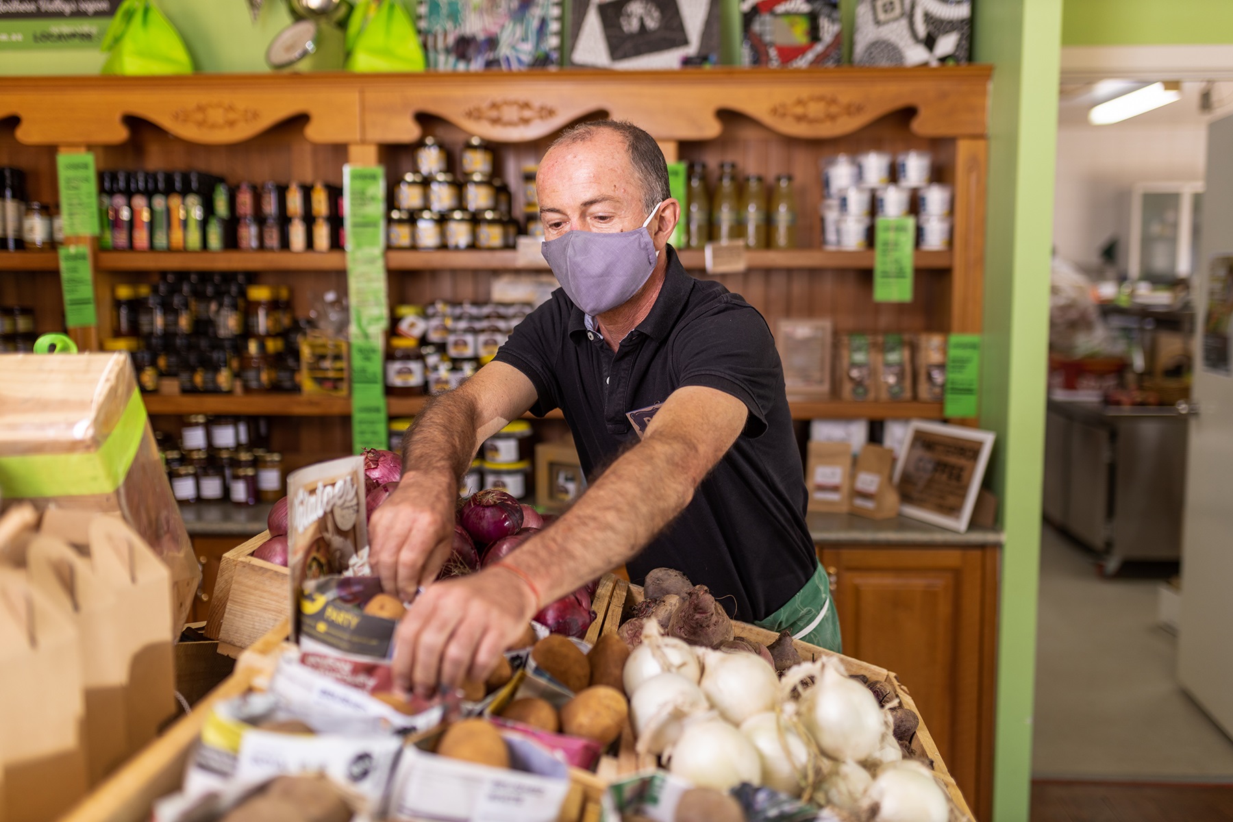 Photo of a man arranging a display of vegetables in a food business. He is wearing a mask as part of COVID-19 health and safety protocols.