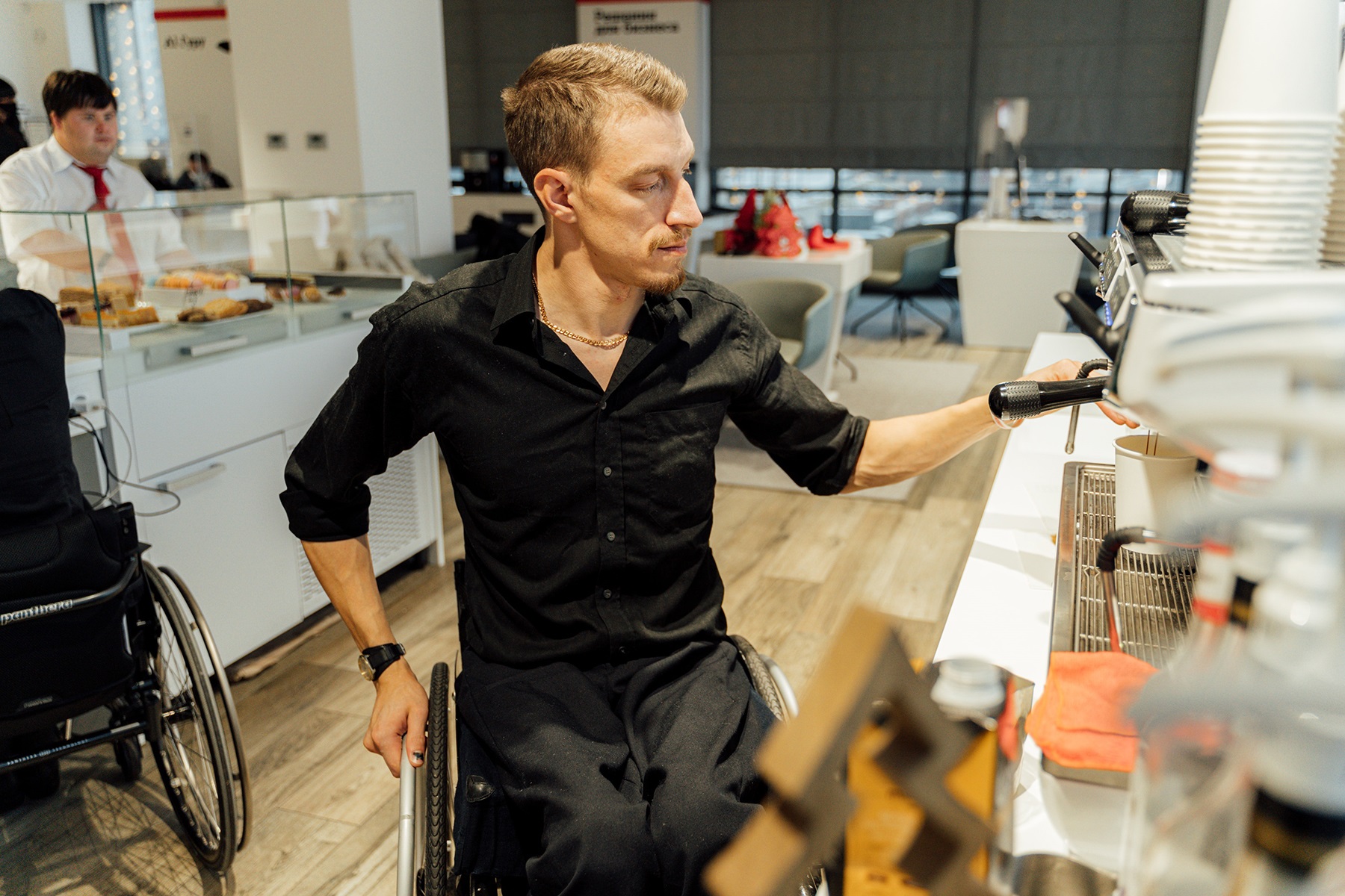 Photo of a man in a wheelchair using a coffee machine in a cafe.