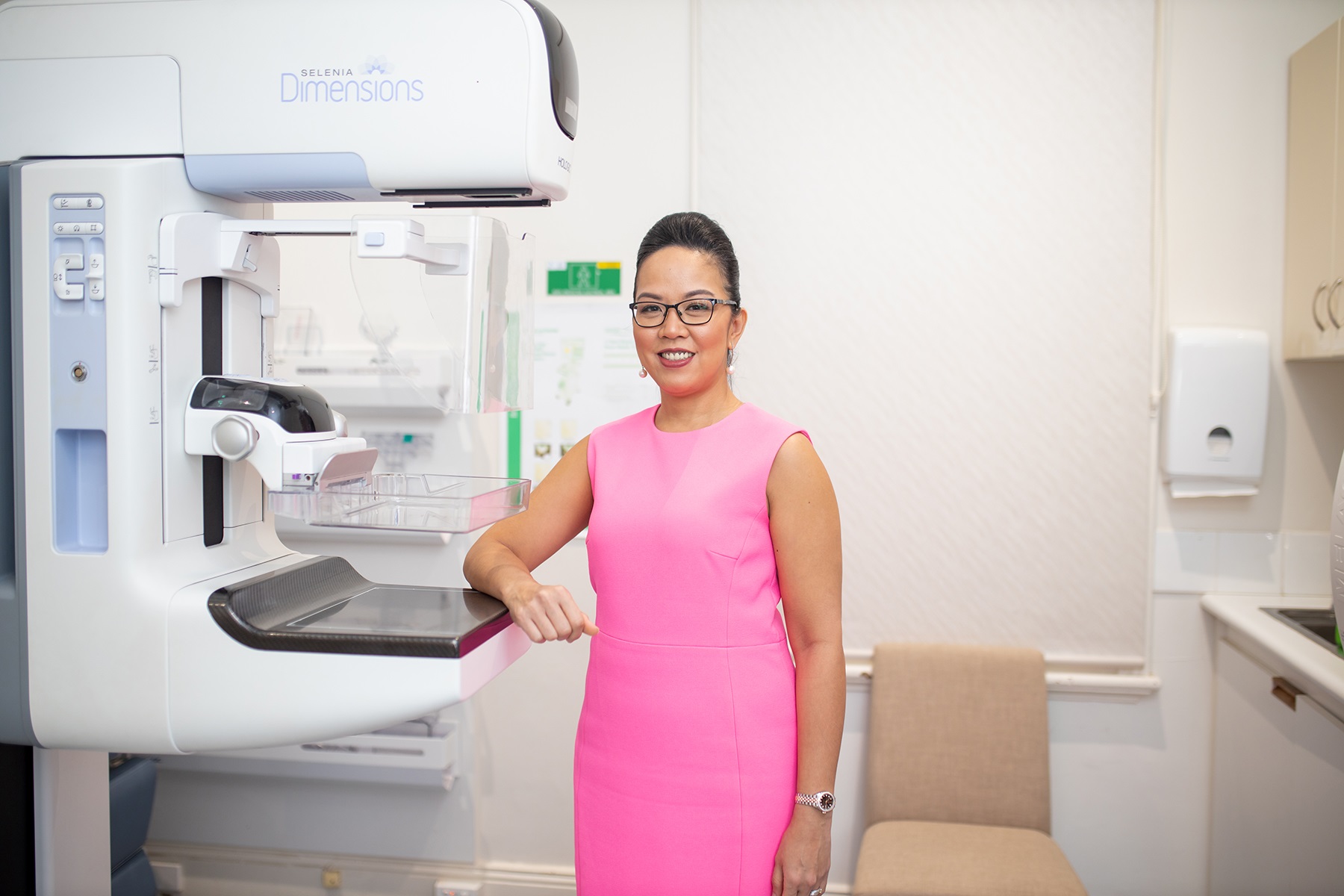 Photo of Dr Vanessa Atienza-Hipolito. She is standing next to a mammography machine in her business, Women’s & Breast Imaging.
