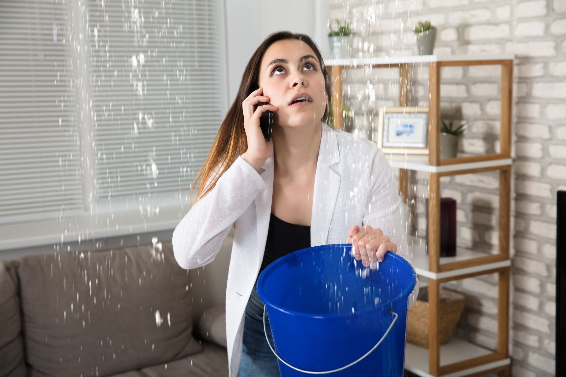 Photo of a woman holding a bucket under a leaking roof.