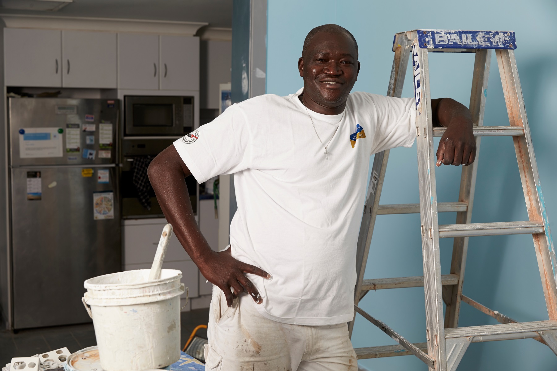 Photo of a house painter standing next to a ladder and a paint bucket.