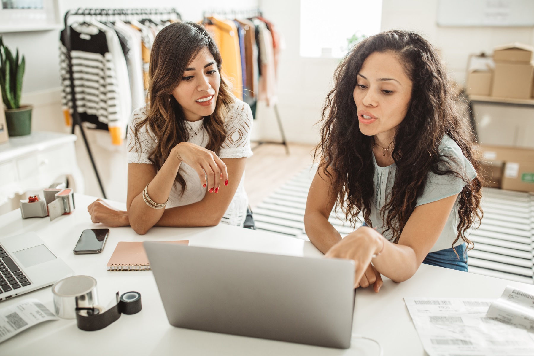 Photo of two women in their clothing business. They are sitting at a table and reviewing information on a laptop.